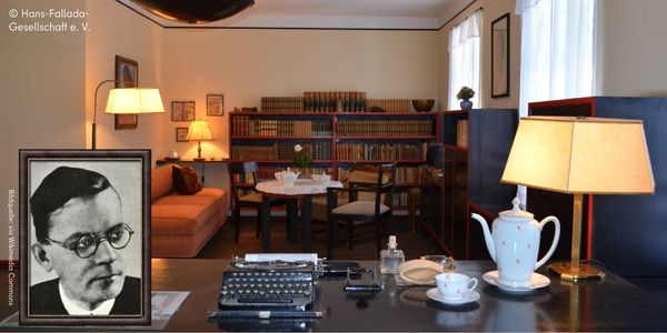 Foto eines Schreibtisches mit SChreibmaschine und Teeservice mit Blick zu einem Bücherregal. Links ist das portraitfoto von Hans Fallada zu sehen.